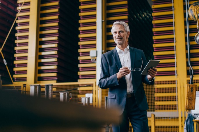 Mann steht in einem Werk und hält ein Tablet in der Hand